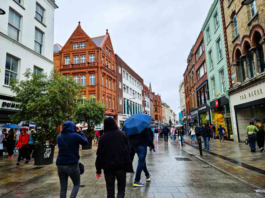 A picture of people walking on Grafton Street on a rainy day in Dublin with umbrellas and hoods visible.