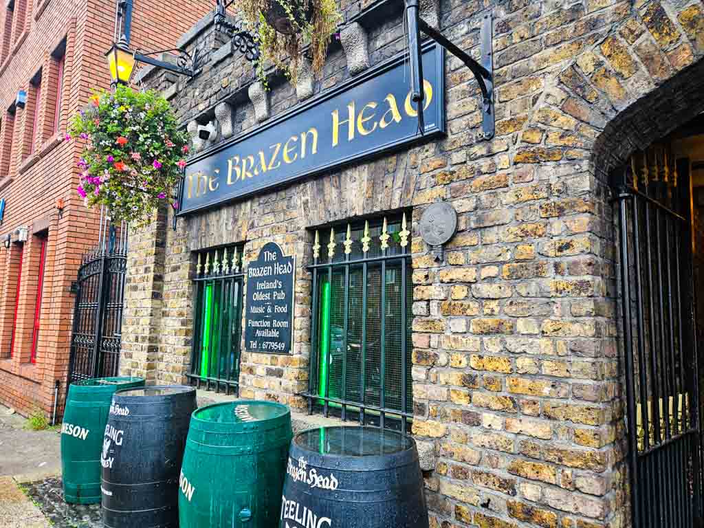 A picture of the exterior and sign of the Brazen Head in Dublin with four barrels outside and a small part of the entrance gate visible.