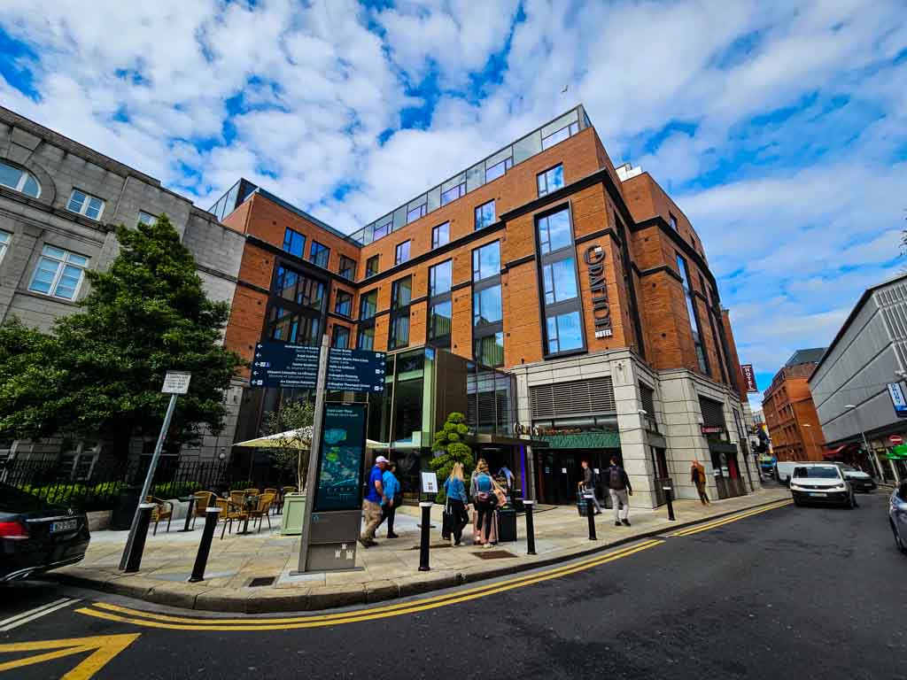 A picture of the Grafton Hotel in Dublin City Centre with blue skies overhead and people walking along the pavement outside.