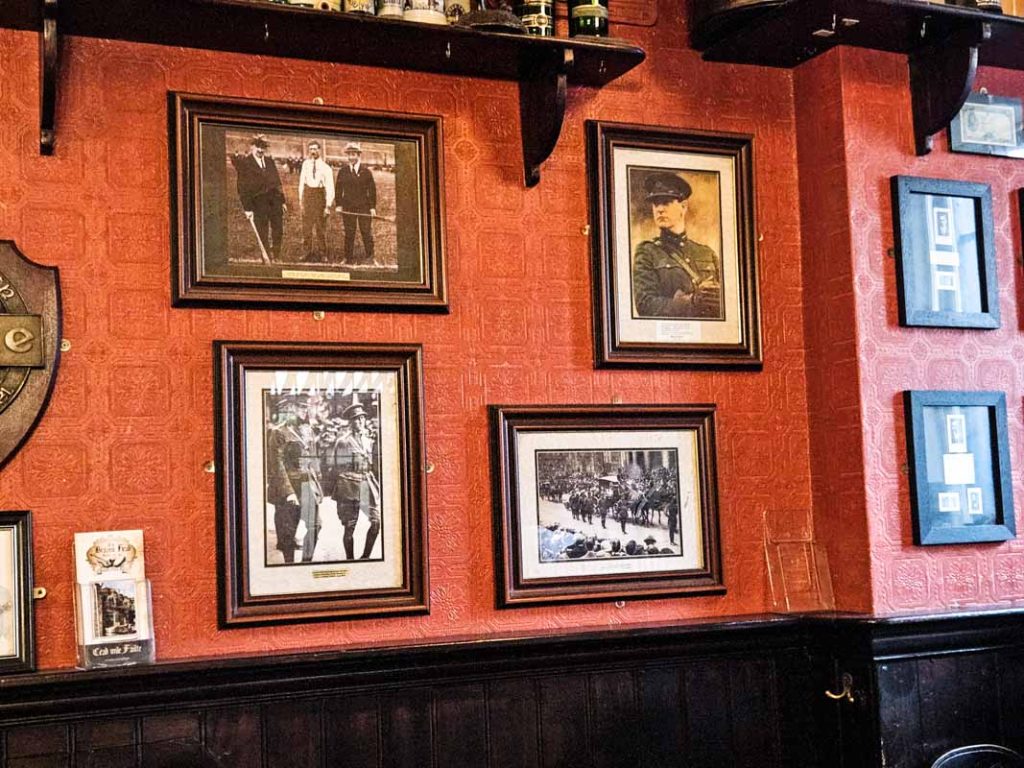 Michael Collins pictures on the wall of The Brazen Head pub in Dublin. The wall is red and the picture are sepia and in brown wooden frames. There are four picture on the main wall.