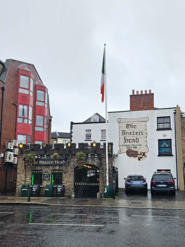 A picture of the exterior of The Brazen Head, Dublin's oldest pub with grey skies above it and the Irish flag on a pole.