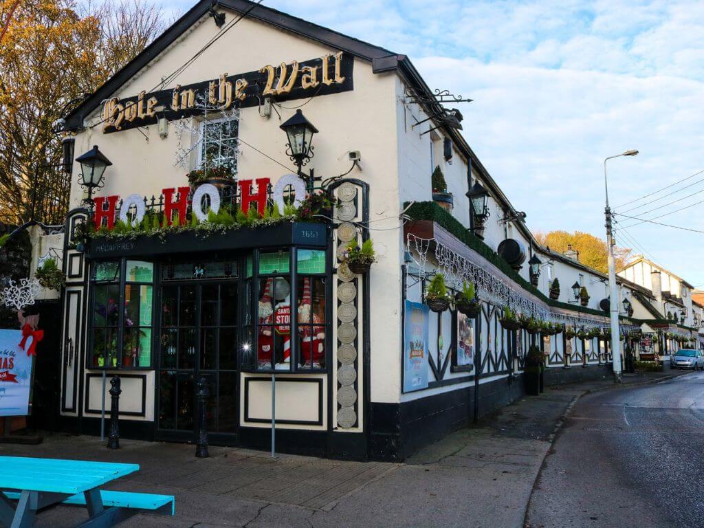 A picture of the exterior of The Hole In The Wall pub in Dublin. There is cloudy blue skies overhead and the pub is cream in colour with black trim.