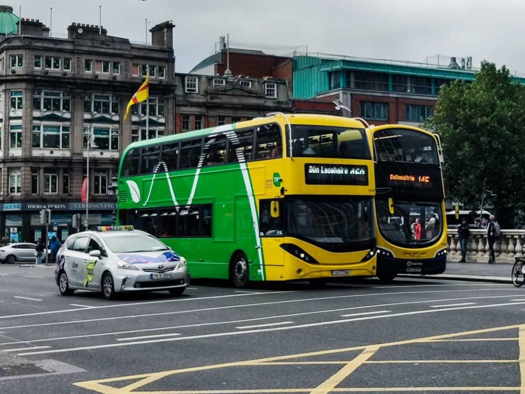 A picture of two Dublin Buses and one taxi on O'Connell Street during a grey and rainy day in the city.