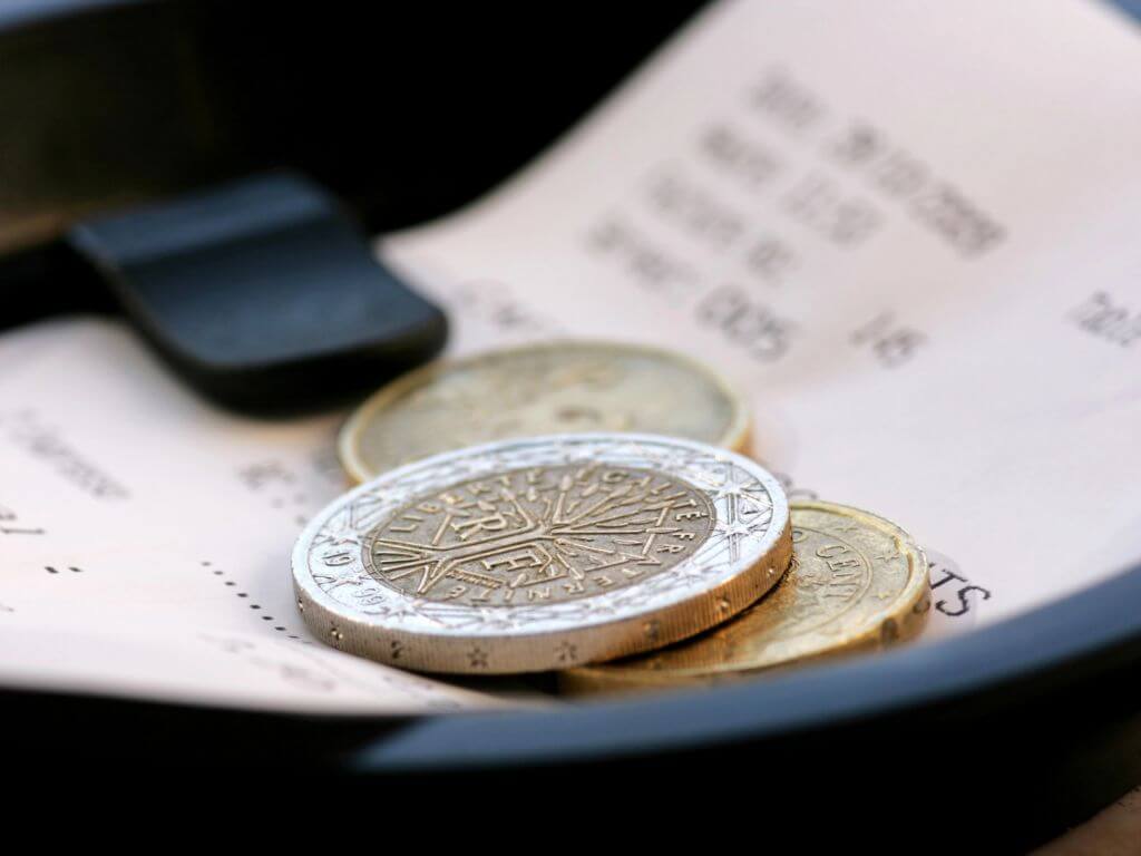 A picture of a restaurant bill plate, with a receipt tagged under the holder and some euro coins sitting on top of the receipt, perhaps being left as a tip.