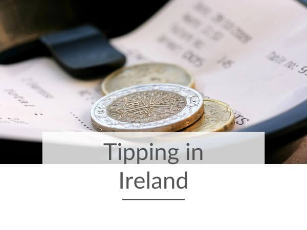 A picture of some euro coins sitting on top of a receipt on a bill plate with text overlay saying tipping in Ireland.