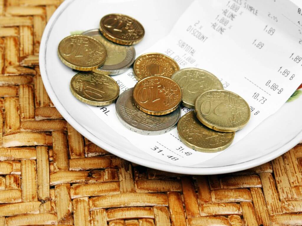 A white plate on a wicker table with a bill and some loose change on the plate, which may be left as a tip.