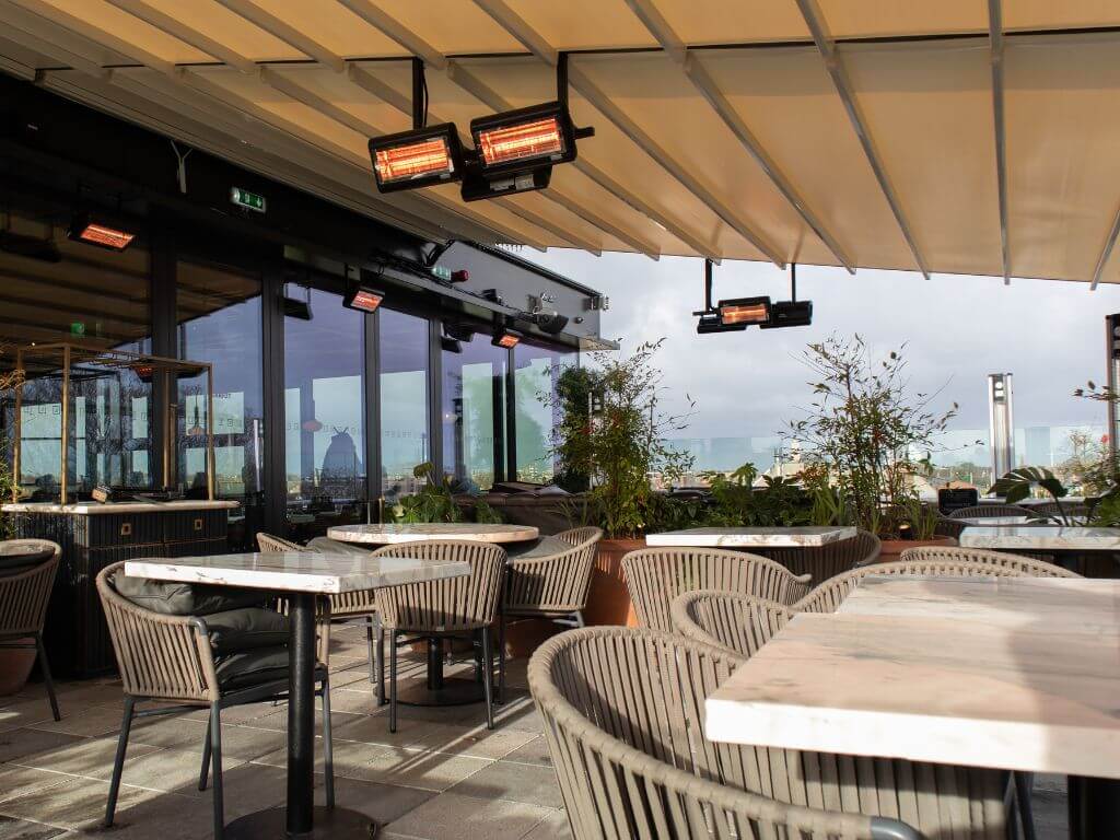 A picture of part of the terrace at Layla's Rooftop Bar at The Devlin Hotel, Dublin with square tables and wicker chairs set out and a cream coloured roof covering over them.