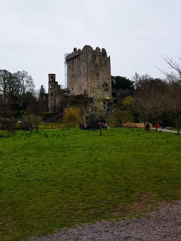 A picture of Blarney Castle in County Cork with grass in the foreground and grey skies overhead.