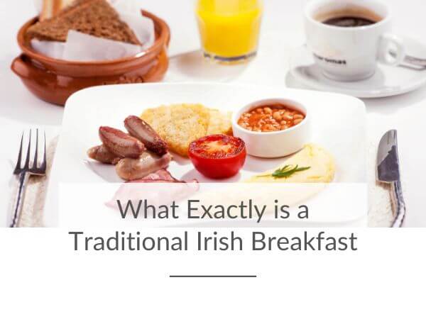 A picture of an Irish breakfast plate with bread, orange juice and coffee in the background and text overlay along the bottom of the picture saying what exactly is a traditional Irish breakfast?