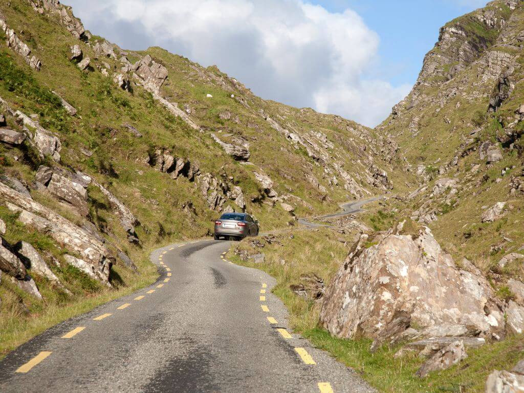 A picture of a car driving along the Ballaghbearna Gap Road in the Killarney National Park.