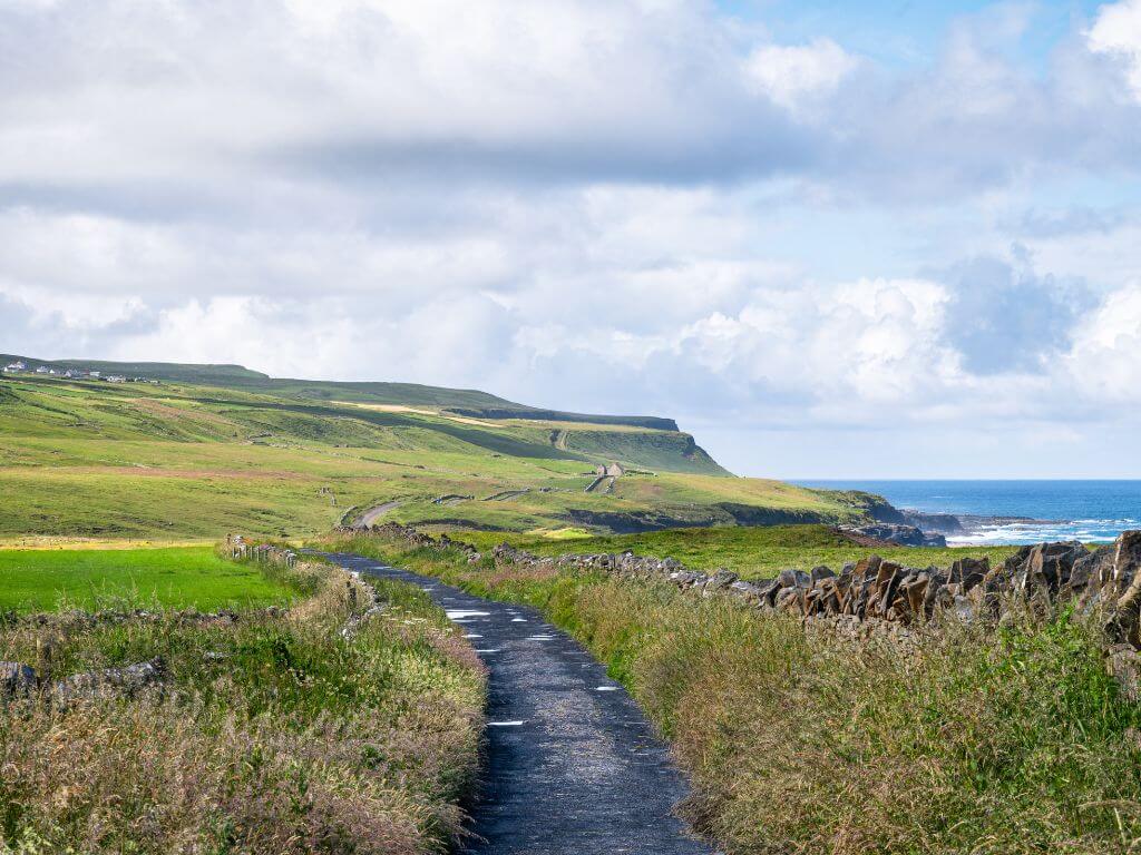 A picture of a country road to the Cliffs of Moher in Ireland. It is a single track road with fields and stone walls along either side.