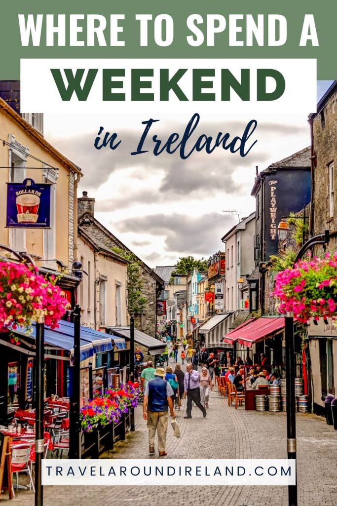 A picture of street in Kilkenny, Ireland with slower baskets in bloom on the street poles and people wandering the street, and text overlay saying where to spend a weekend in Ireland.