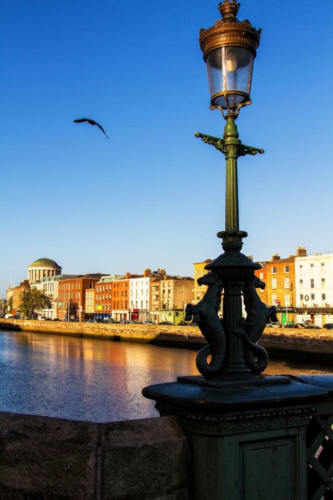 A picture of a riverside light along the River Liffey in Dublin, with the top of the Four Courts building visible in the distance and the quays in the background.