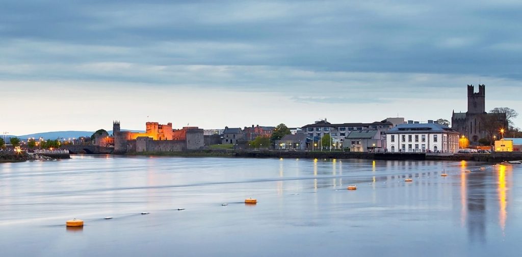 A picture looking at Limerick City across the River Shannon, with King John's Castle visible on the far left across the banks, and St Mary's Cathedral on the far right.